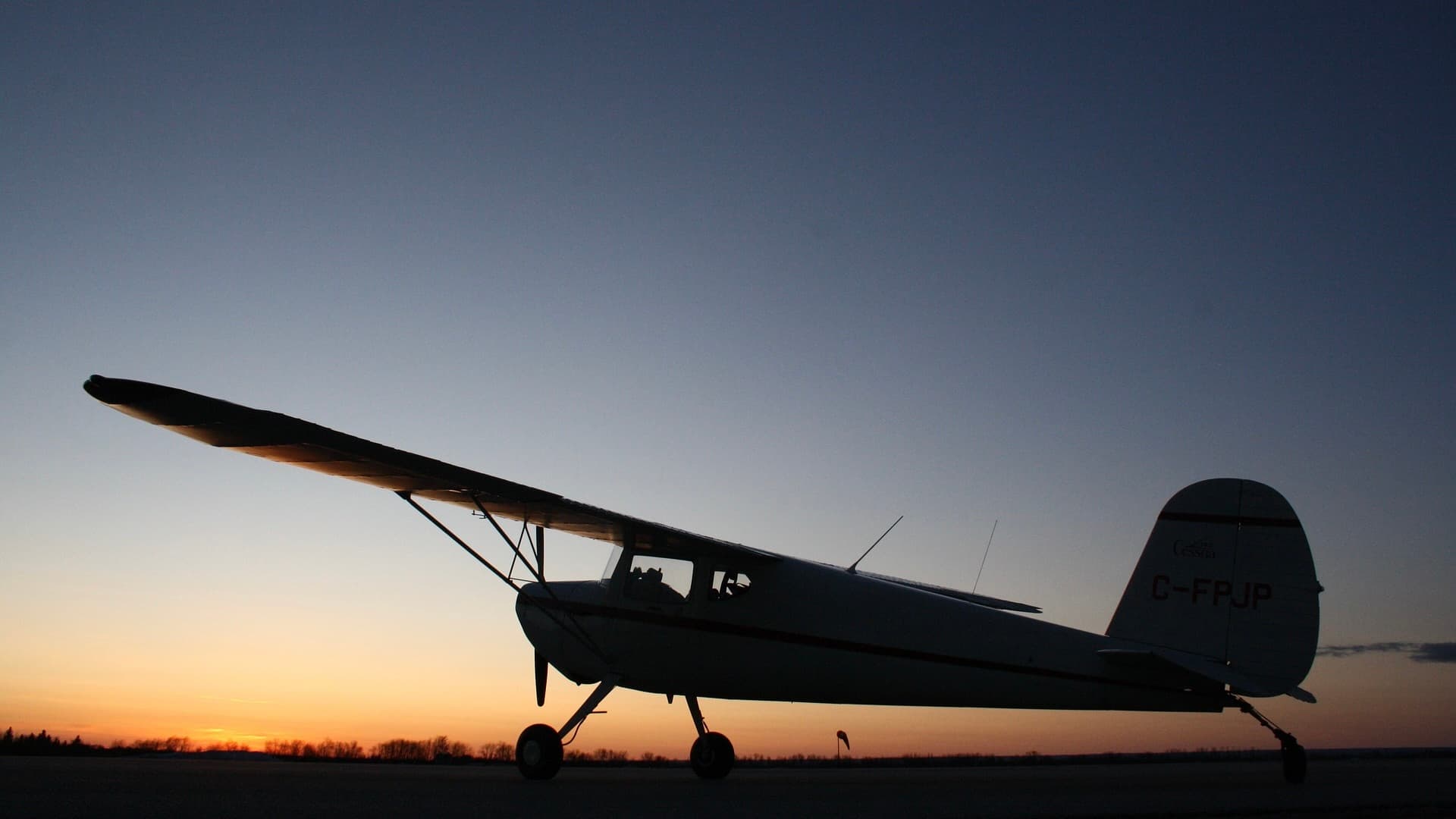 A small airplane on the ground with the sun setting in the background.